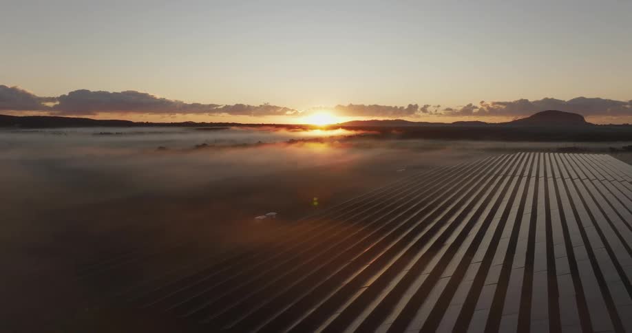 A sunrise casts a golden glow over a vast geometric field of solar panels