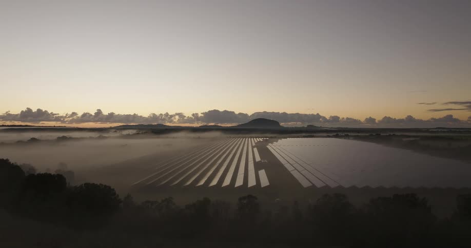 Fog partially covers solar panels at a solar farm while red tints the horizon