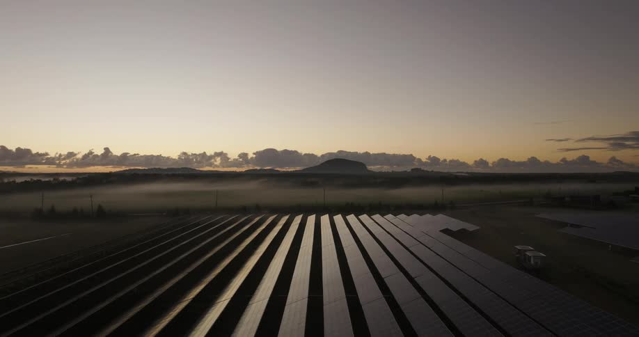 Vehicles driving along a country road pass a foggy field containing rows of solar panels
