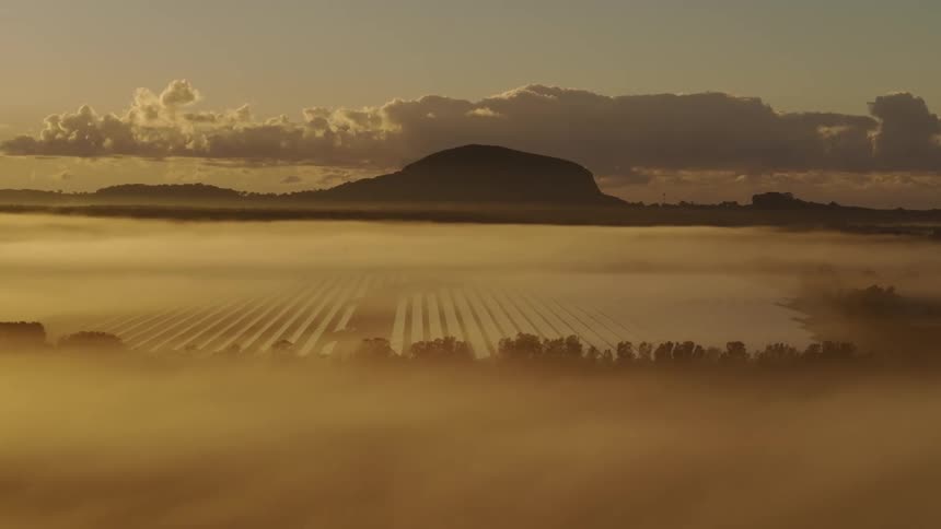 Dense fog settling in a valley as the sun rises on the horizon over mountains on the horizon