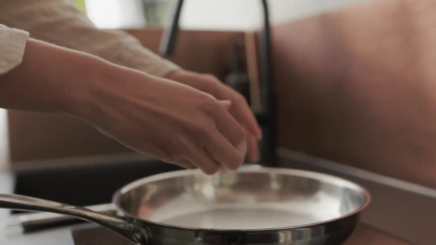 An adult breaks an egg into a frying pan on the stovetop