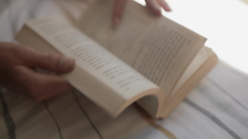 A woman outdoors turns a page in a book