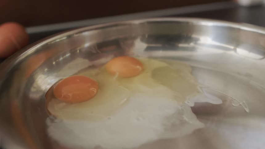 You are absolutelya persons hands are shown cracking an egg open pouring the yolk and white into a frying pan
