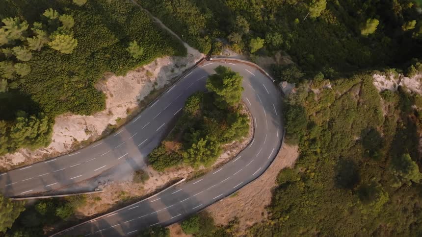 An aerial view of an asphalt street with a motorcycle passing by making a sharp turn