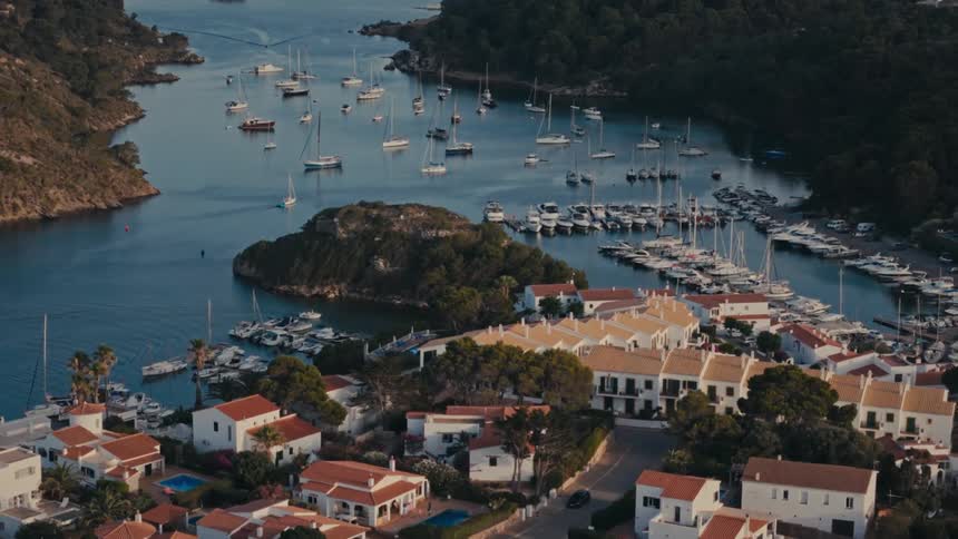 An aerial view of a coastal town with several boats and marina on the water and the houses are all white in color with orange colored roofs