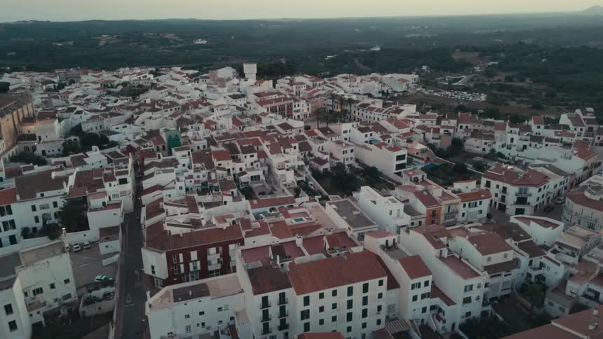 Birds fly over red roofed apartment buildings near a landmark building in a town surrounded by trees