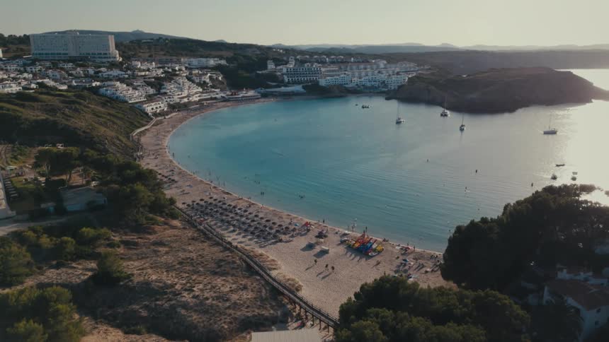 People walk on a beach by a city and bay