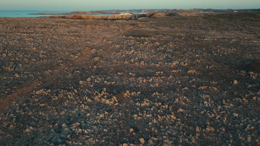 An aerial of rocky terrain glowing in the sunset near the coast