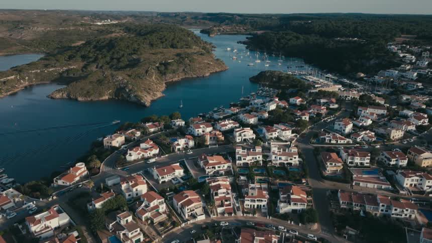 An aerial view of a coastal town with a bay full of boats and the town houses are all white in color
