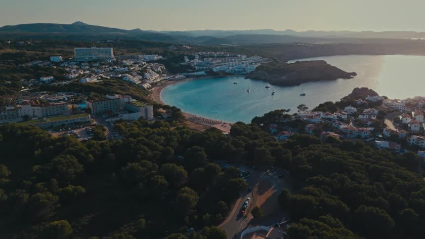 Boats sit in a bay by a beach and a small city with suburbs