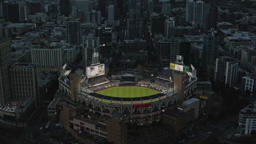 An aerial view of a large grass sports stadium in a metropolitan city at night