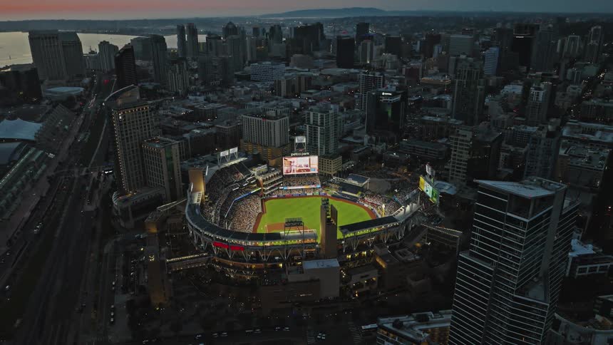Sports fans fill a brightly lit stadium after dusk in a coastal city