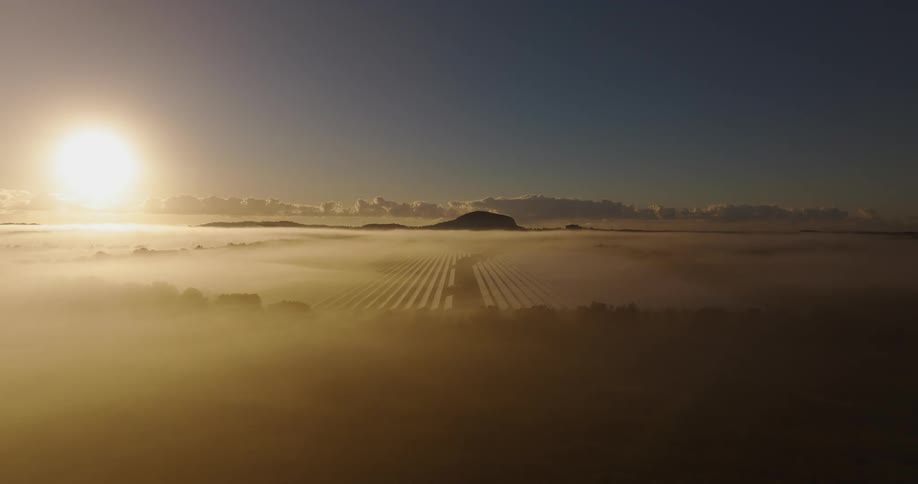 An aerial view showed a solar panel farm with heavy fog hovering over the site and a mountain in the background