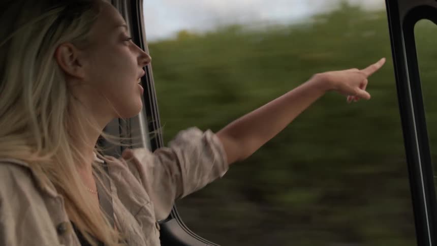 A woman points outside the window while riding in the vehicle