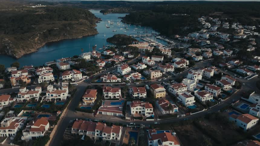 A city facing a bay of water full of boats and the houses in the cities are all white with orange roofs