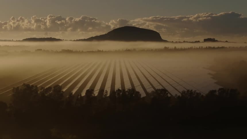 Solar panels sit on a plain near forests and a distant mountain range