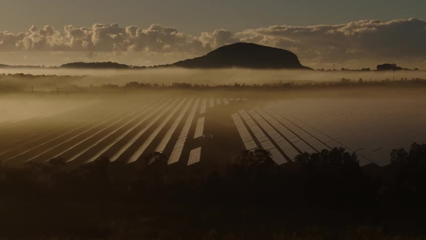 Solar panels partially fill a large plane situated between a mountain range and a forest