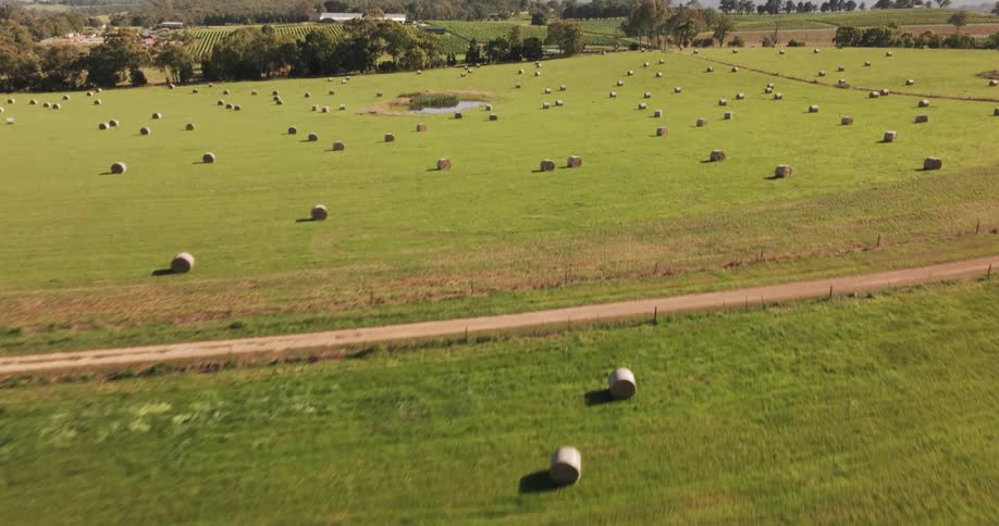 Dirt roads pass fields dotted with hay rolls in the rural countryside