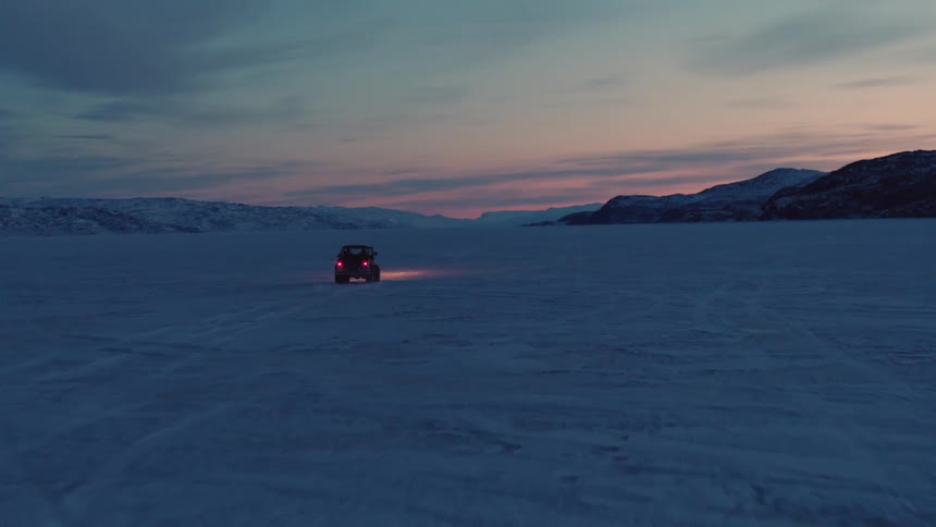Vehicle drives across snow covered field after sunset