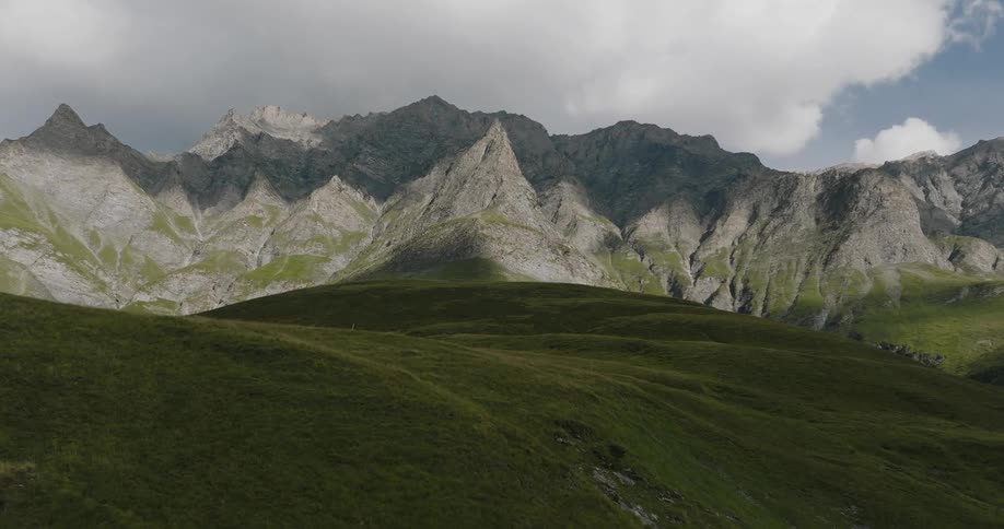 A view of a landscape of a grassy hill and in the background a range of rocky mountains