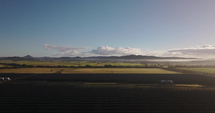 A large farm of solar panels pointing towards the sky on a clear day with some white clouds