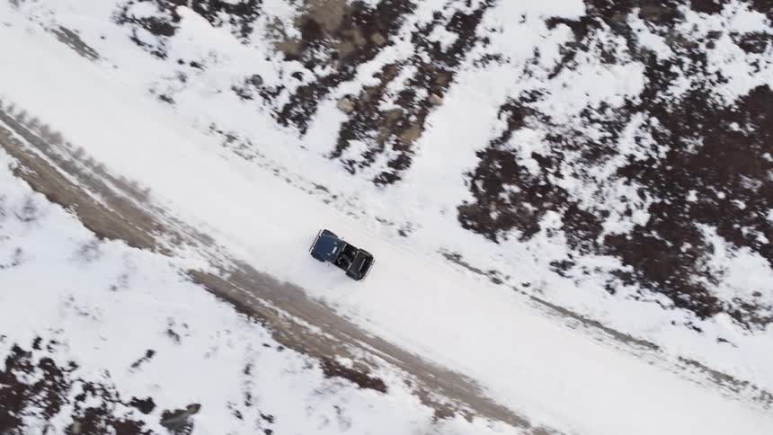 A vehicle drives on the snow filled dirt road