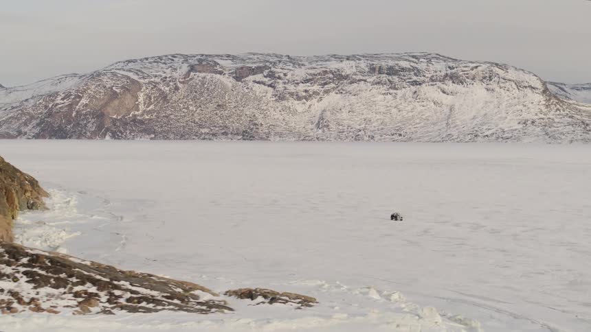 A small car driving on snowy ground in a region with snowcapped mountains
