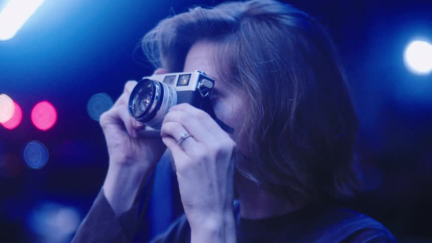 A woman stands in a city and takes photographs with a camera