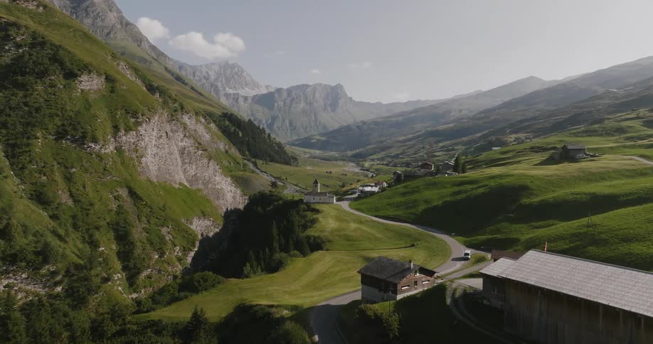 Road winds through a conifer forest and a town separated from a steep mountain cliff by a ravine