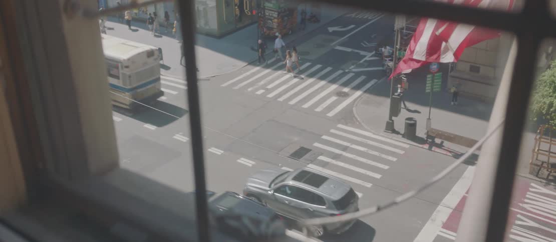 Aerial view of a city street from behind a window with pedestrians crossing the street and vehicles at an intersection