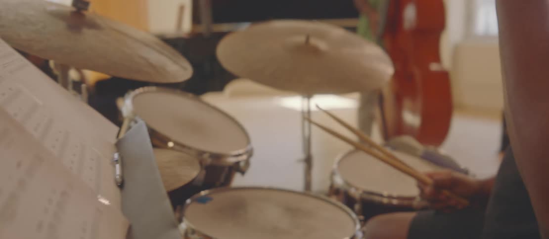 A man is sitting in front of a drum set and he is making a note on a piece of paper and he puts it in front of him and then he starts shaking his head up and down