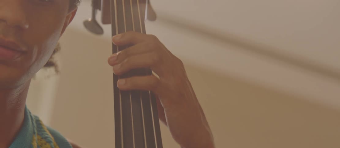 Closeup of fingers on the strings of a double bass with a partial view of the players face