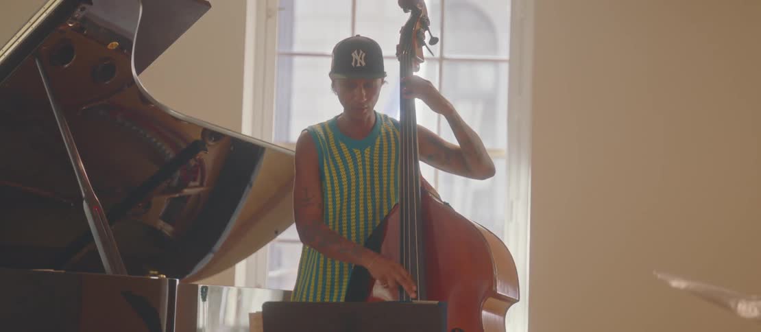 A man in a green and yellow tank top is playing the celo violin and is nodding his head up and down