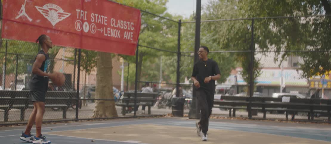 Two male friends play basketball on an outdoor court near a busy street
