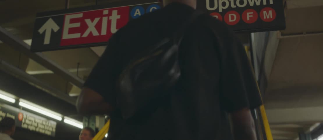 Man with backpack walking through crowd of people towards a staircase at a train station