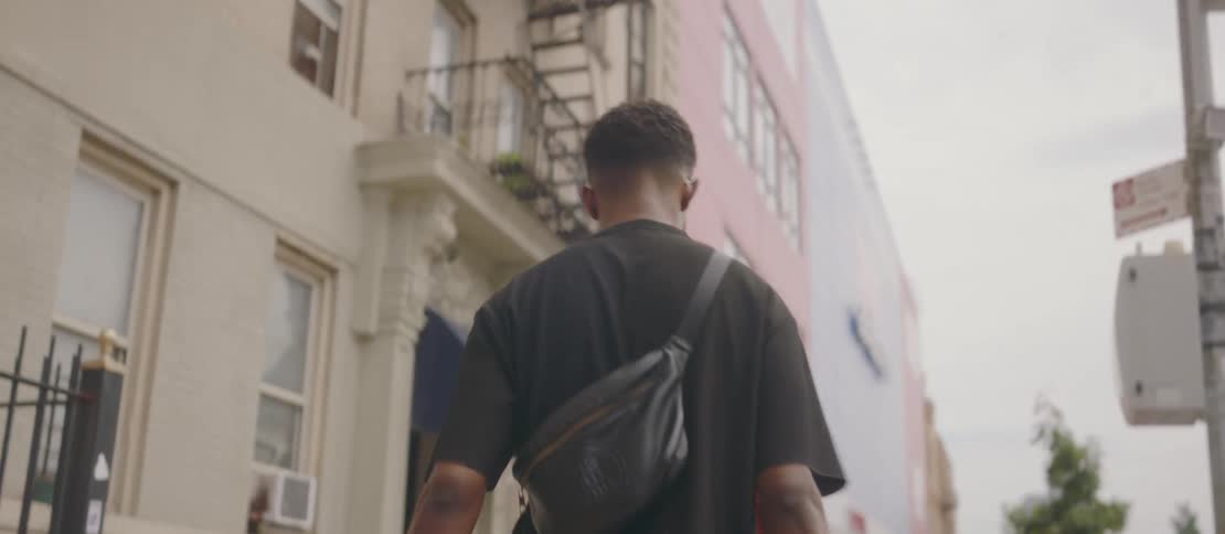 A young black man walks down a city street while carrying bags