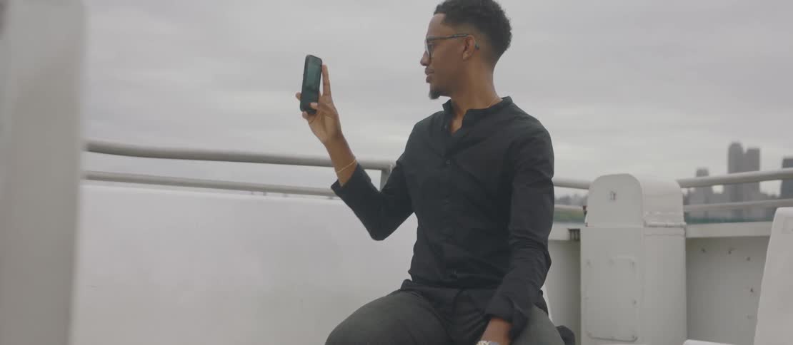 Man sitting on the outside of a boat filming with his iphone around