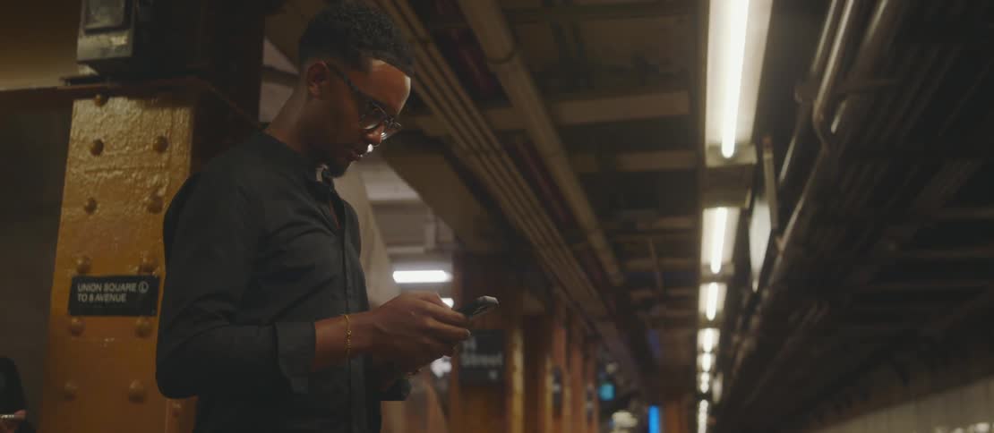 Man waiting at a public transit station uses his smartphone