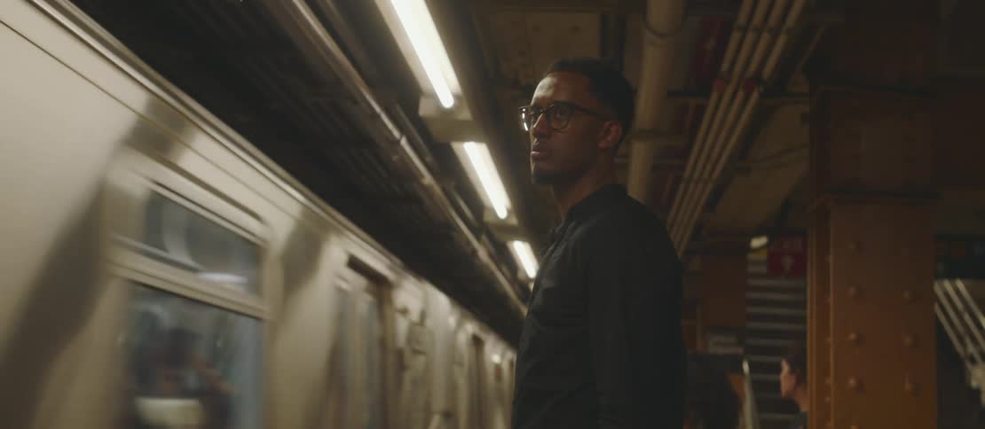 Man in a subway station taking out his cell phone as a train passes in front of him