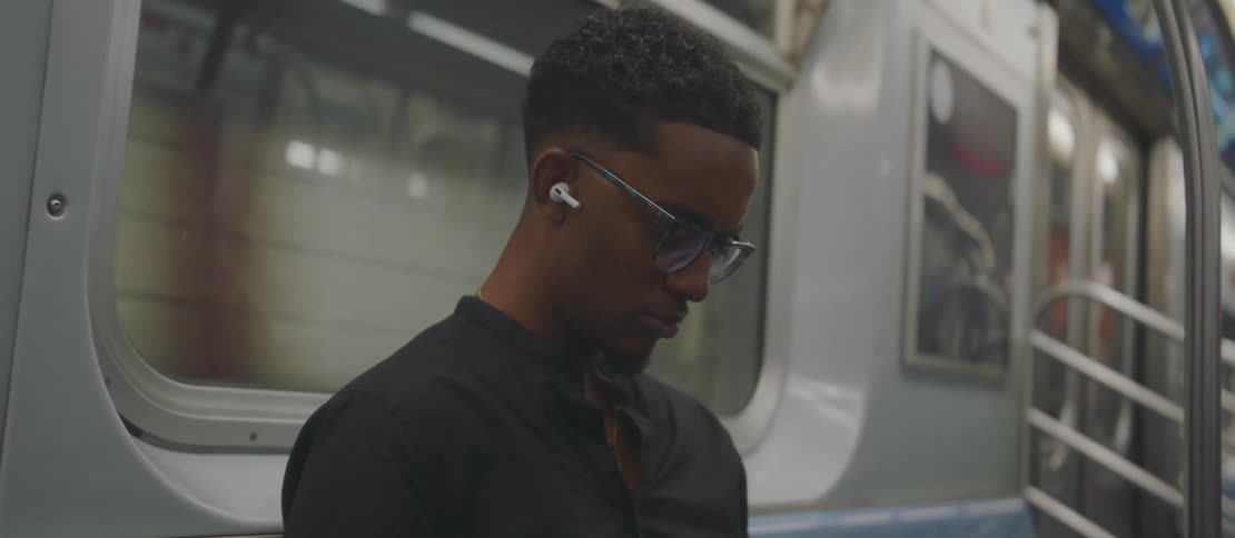 A young man inside a subway train listening to music on his smartphone