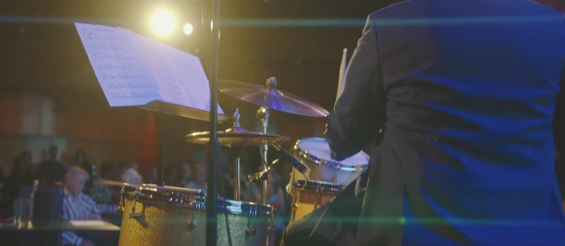 Two black men perform in a band to an audience in a concert venue