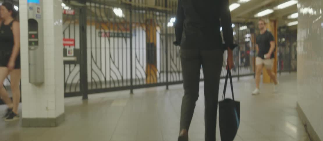 A man with reading glasses wearing dress shoes and holding a black bag is walking in a terminal