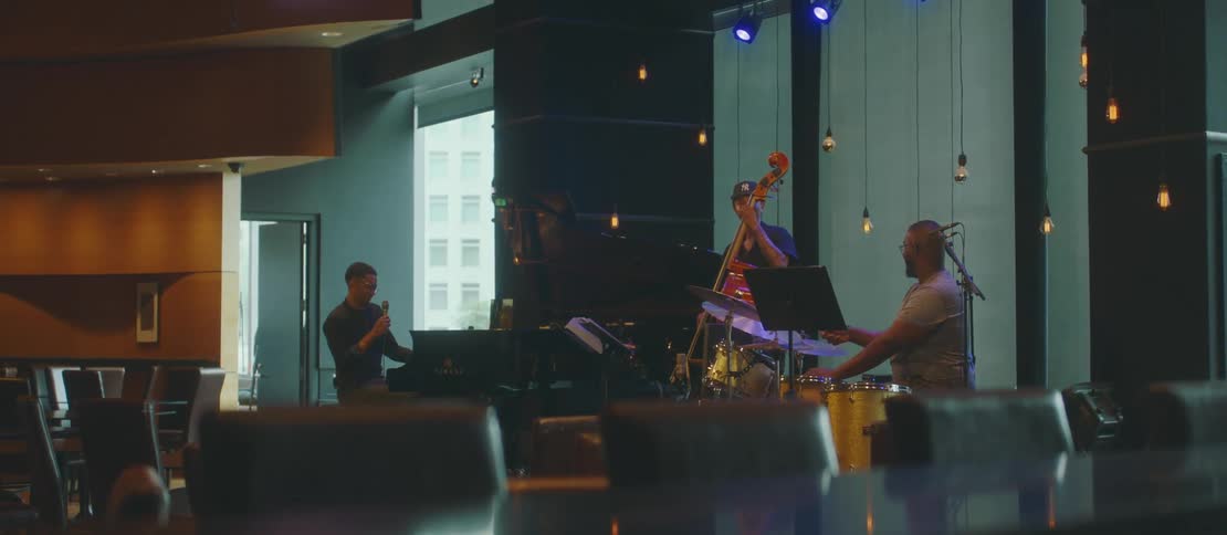 Musical group in a rehearsal including a violinist drummer and a singer in a sitting at a piano