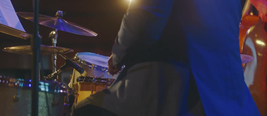 Closeup of a drummer wearing a blazer performing on stage under colorful lights