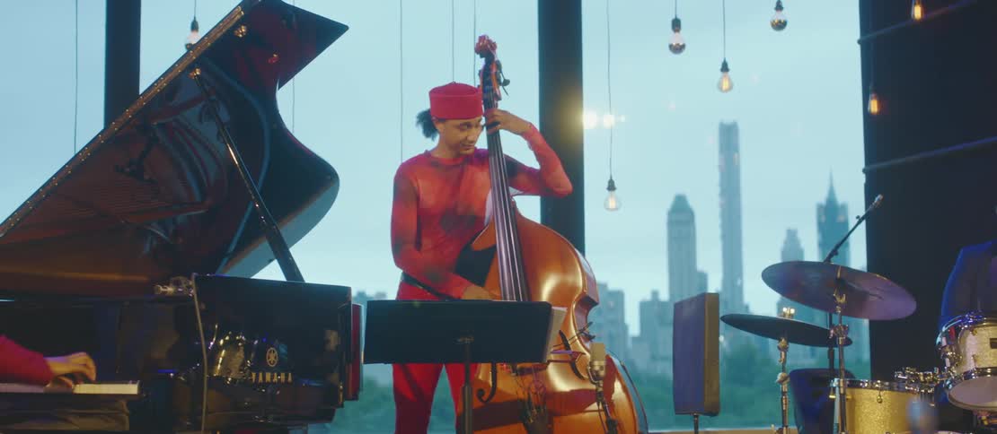 A man standing playing a violin celo next to a piano and a drummer