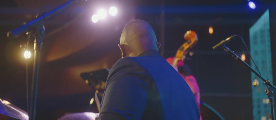 A man plays the drums on stage with his bandmate in front of a small audience