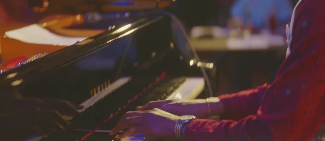 A young black man plays piano onstage for a crowd of people