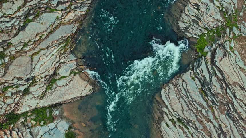 A small stream with fast water that runs in the middle of a very rocky coast