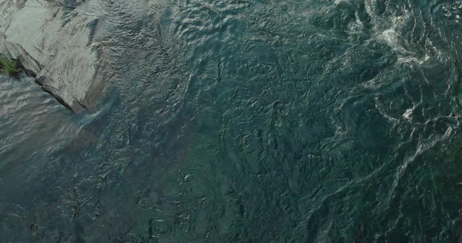 An aerial view of a fast flowing river cuts through gray sedimentary rock