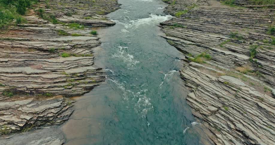 Aerial view of a river cutting through layered rock formations with trees lining the edges